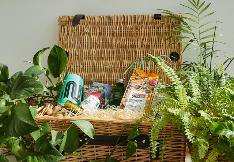A wicker hamper of ethically sourced products surrounded by green foliage